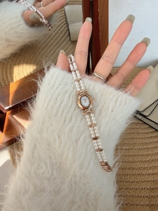 Detail of vintage oval watch with rose gold case and double-row pearl strap on wrist