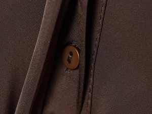 Detail view of smooth dark brown poplin fabric with matching round button and stitching