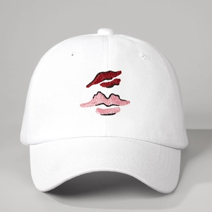 Close-up of white cotton baseball cap featuring detailed red and pink lip embroidery on crown