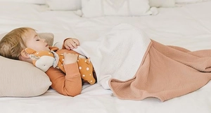Detail of baby cotton gauze blanket with waffle texture and plush deer toy on white bed