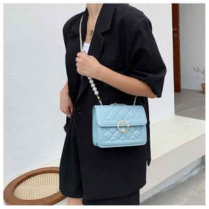 Close-up of quilted light blue PU leather bag with pearl handle and metal ring buckle