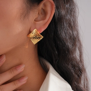 Close-up of gold geometric rhombus stud earrings with textured surface on model