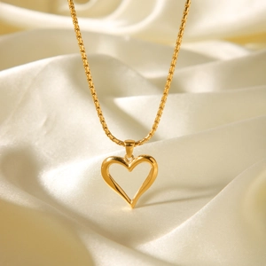 Detail of a hollow heart pendant on a gold chain over champagne silk fabric texture