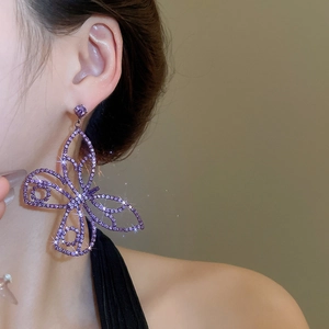 Close-up of model wearing large purple hollow butterfly earrings with sparkling cubic zirconia