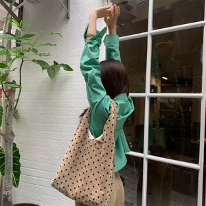 Outdoor shot of a brown polka dot corduroy tote bag worn by a model in a green shirt