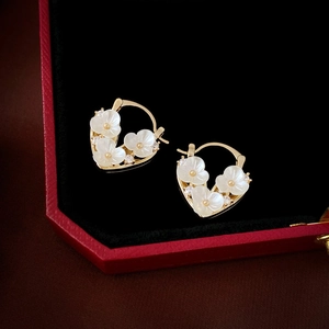 Close-up of golden heart earrings with white flowers and zircons in a red jewelry box