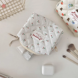 Trousse à maquillage matelassée à motif cerise avec pinceaux sur un bureau blanc.