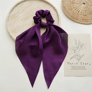 Detail of elegant dark purple satin hair scrunchie with long ribbon on a stylish tray