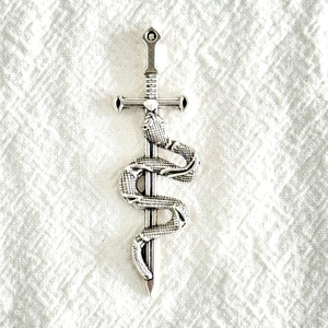 Pendentif épée et serpent en alliage argenté vintage sur fond de tissu blanc