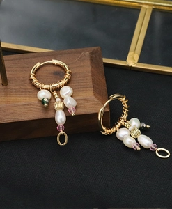 Detail view of baroque pearl earrings with gold rings on a premium wooden base stand