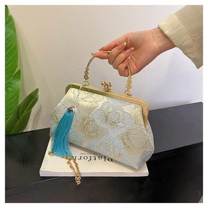 Detailed close-up of embroidered floral pattern and blue tassel on beige shell bag