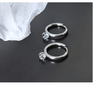 Detail of silver hoop earrings with sparkling round zirconia pendants on dark background