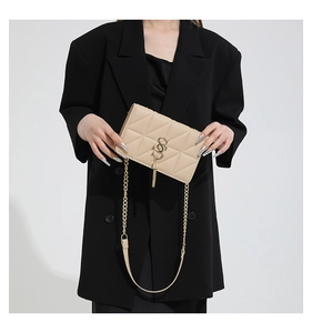 Detail of beige quilted flap bag with golden metal logo and elegant tassel charm