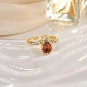 Macro shot of gold ring with teardrop orange gemstone and diamond inlay on white ripple