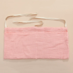 Detail of pink cotton gauze baby organizer showing dual pockets and white tie straps