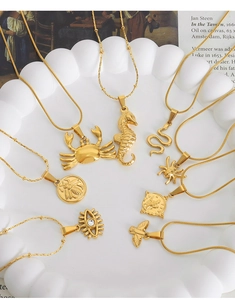 Collection of gold animal pendants including crabs and bees on white cloud ceramic tray