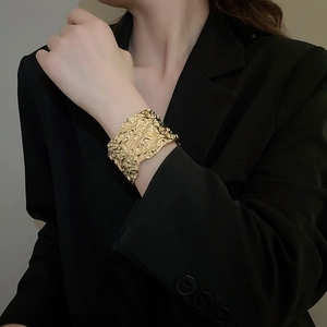 Detailed view of wide gold irregular textured cuff bracelet on model wearing black