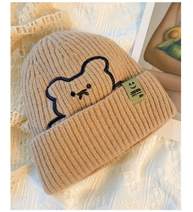 Detail of khaki knit beanie with bear embroidery and side label on soft background