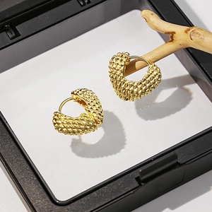 Détail de boucles d'oreilles cœur doré avec texture tressée sur une branche en bois