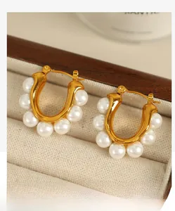 Detail of gold U-shaped earrings with six elegant white pearls on wooden jewelry box