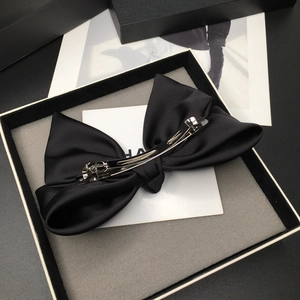 Detail of elegant black satin bow hair clip with glossy finish in a luxury gift box