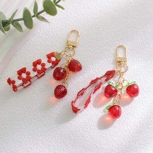 Detailed close-up of strawberry keychain with gold lobster clasp and woven floral ribbon