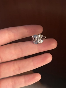Nahaufnahme der silbernen Ohrklemme mit Zirkonia-Kreuzbuchstaben in der Hand gehalten
