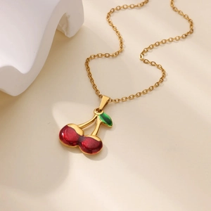 Elegant gold chain necklace with red cherry fruit pendant on a minimalist cream background