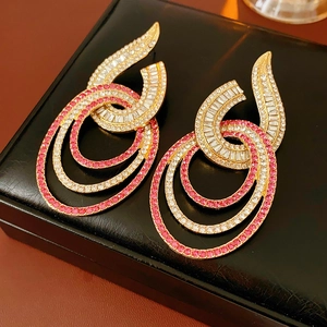 Close-up of golden geometric earrings with white and pink crystals on black leather box