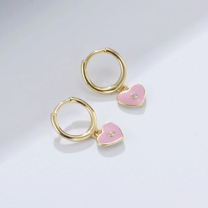 Macro detail of golden hoop earrings featuring pink enamel hearts and sparkling zircon stones