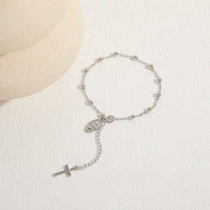Detailed view of silver cross and saint medal pendant on beaded chain bracelet