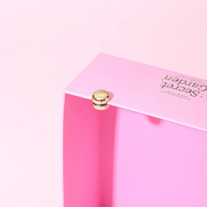 Detail of a pink gift box showing the golden magnetic closure and minimalist typography