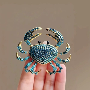 Elegant gold crab brooch with deep blue rhinestones held to show realistic size