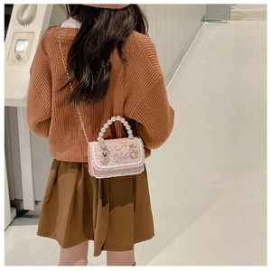 Detail of pink tweed girl's bag featuring elegant pearl handle and floral embellishments
