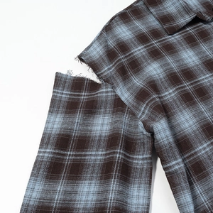 Close-up of cutout shoulder and distressed raw edge on plaid shirt with blue pattern