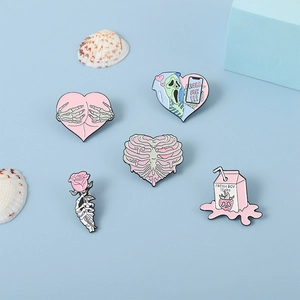 Detail of five enamel pins featuring skull hearts and milk box on light blue background