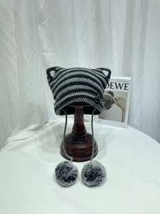 Detail of knitted cat ear beanie with black grey stripes, pom-poms and metal pin decor