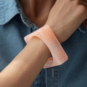 Detail view of wide resin bangle with orange marble texture worn on model wrist