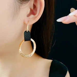 Close-up of golden hammered hoop earrings with black leather texture on a female model