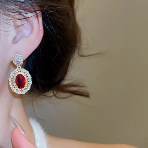 Close-up of gold-plated oval ruby zircon earrings with white stones in vintage royal style