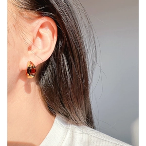 Elegant gold hoop earrings with red emerald-cut zircon stone on model in sunlight