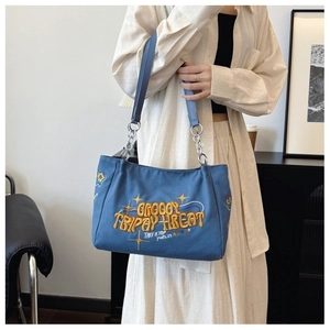 Detail of blue canvas tote bag featuring yellow 3D embroidery and chain shoulder strap