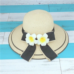 Vue de dessus d'un chapeau de paille beige avec ruban noir et fleurs de frangipanier