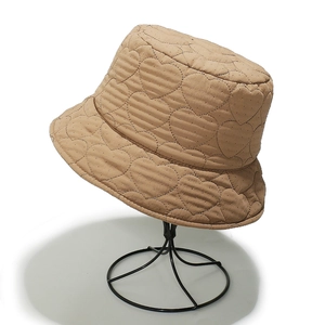 Detail of beige quilted bucket hat with heart pattern on a black display stand