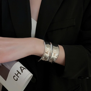 Gros plan sur un bracelet manchette argenté à texture ondulée porté avec un costume noir