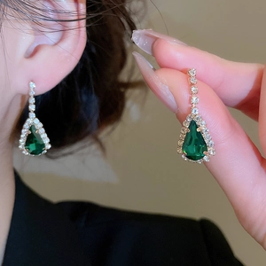 Nahaufnahme luxuriöser vergoldeter Tropfenohrringe mit grünen Steinen und Diamanten