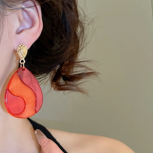 Detailed close-up of water drop earrings in red and orange resin with hammered gold studs