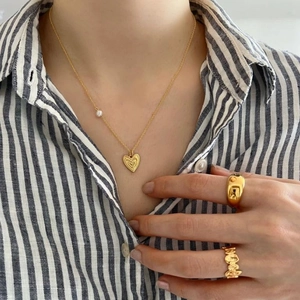 Detail of 925 silver irregular heart necklace and gold rings worn with striped shirt