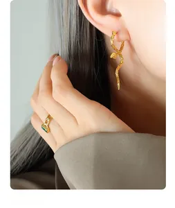 Close-up of elegant gold snake earrings with green gemstone ring on a fashion model