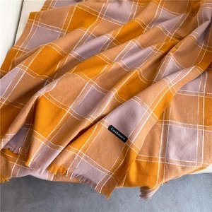 Soft orange and grey plaid cashmere scarf with fringes draped elegantly on a sofa